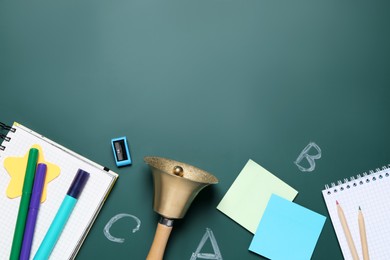 Photo of Flat lay composition with golden bell and school stationery on green chalkboard, space for text