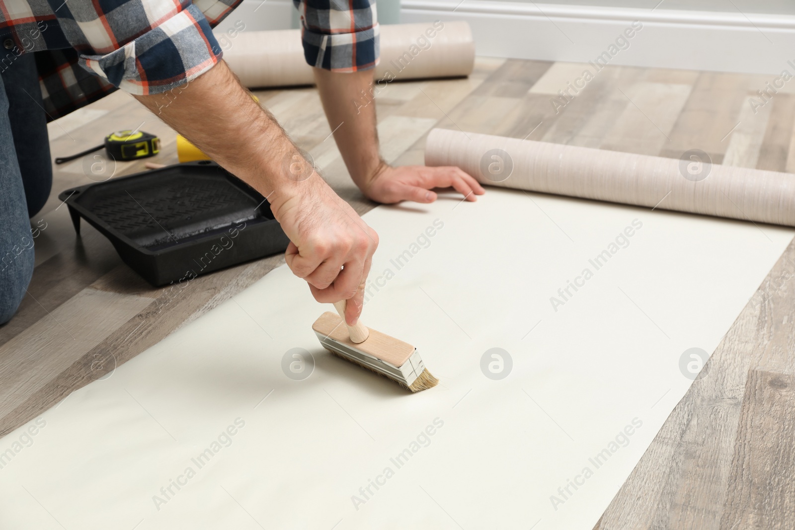Photo of Man applying glue onto wall paper on floor, closeup