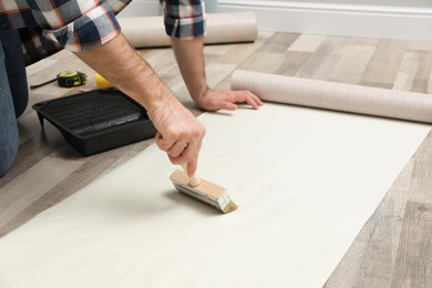 Photo of Man applying glue onto wall paper on floor, closeup