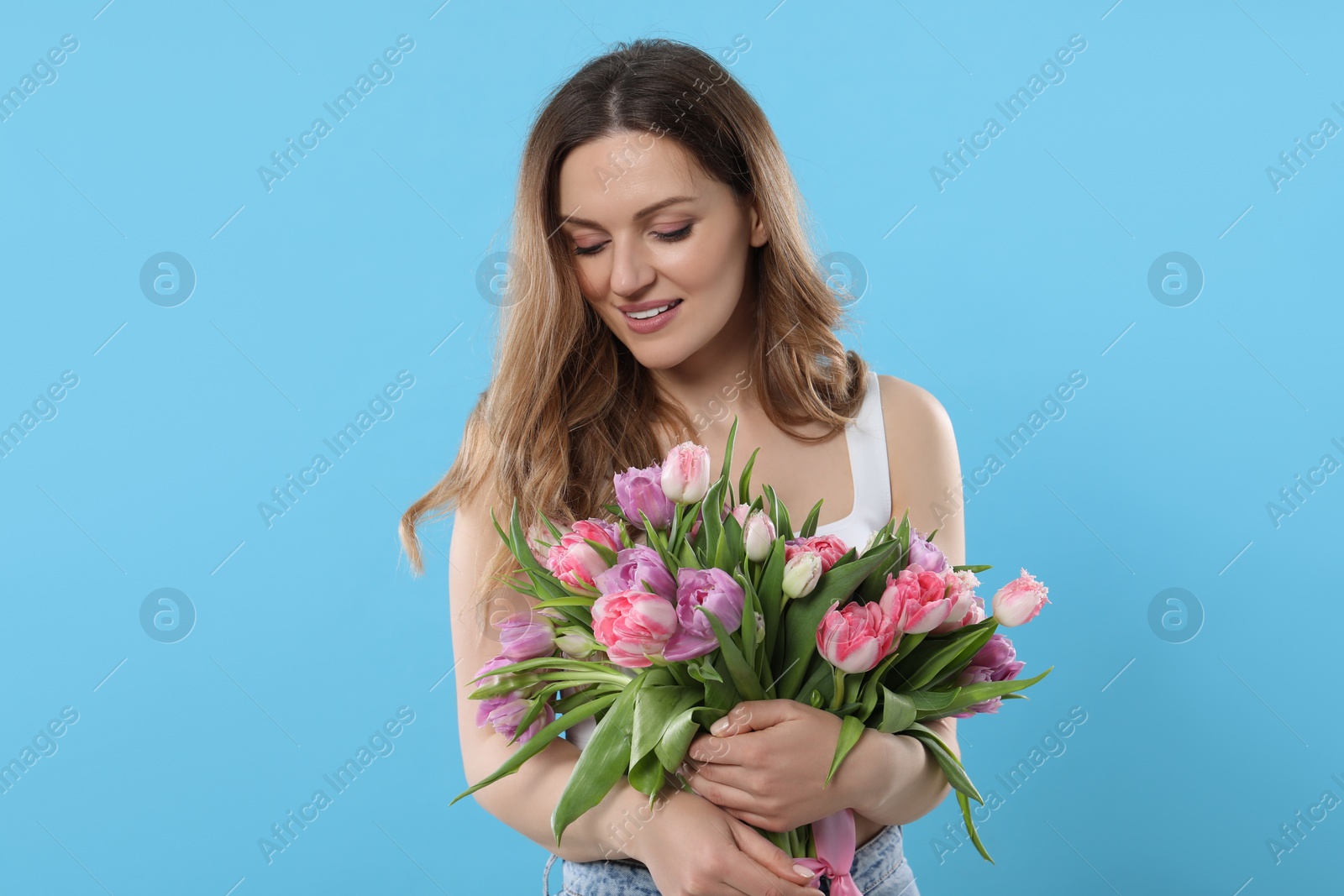 Photo of Happy young woman with bouquet of beautiful tulips on light blue background