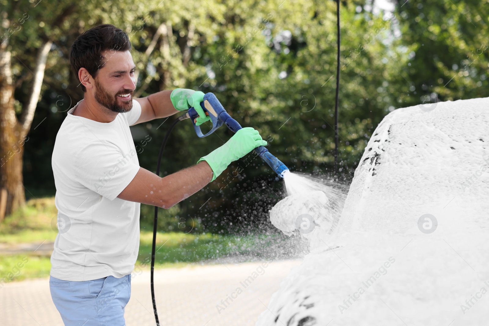 Photo of Man covering automobile with foam at outdoor car wash