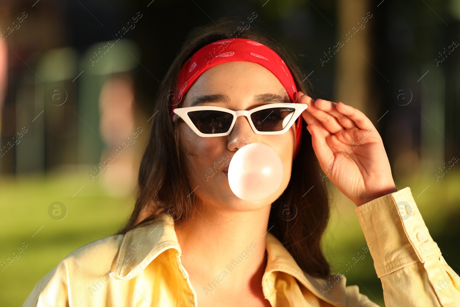 Photo of Beautiful young woman in sunglasses blowing bubble gum in park