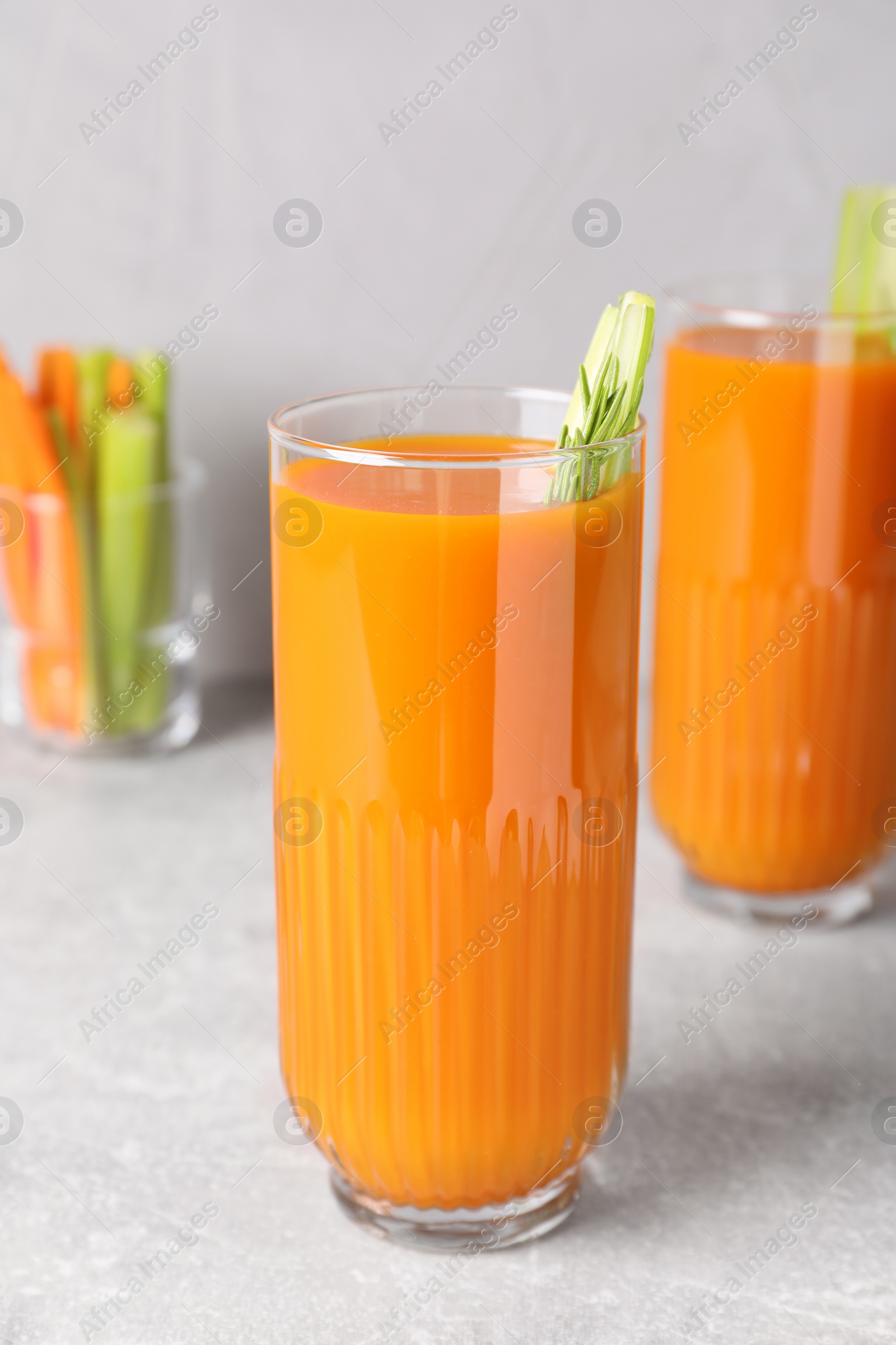 Photo of Glasses of tasty carrot juice with celery sticks on light grey table