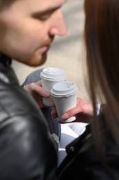 Photo of Lovely young couple with cups of coffee spending time together outdoors, closeup. Romantic date