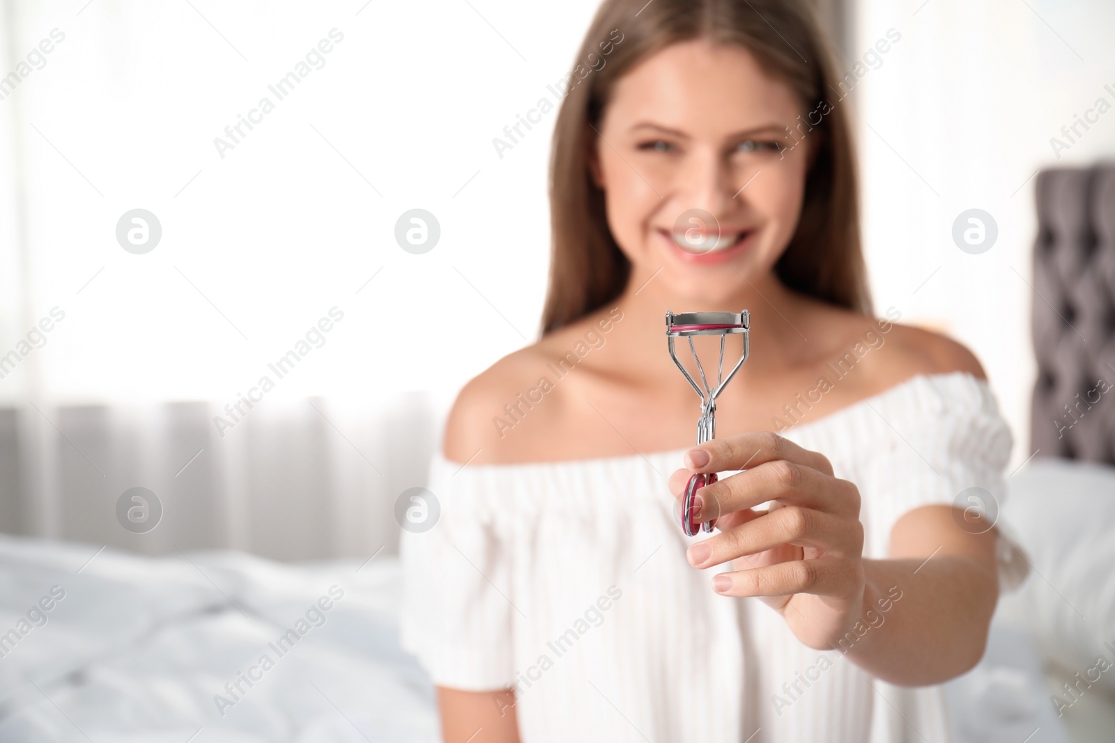 Photo of Young woman holding eyelash curler at home, closeup