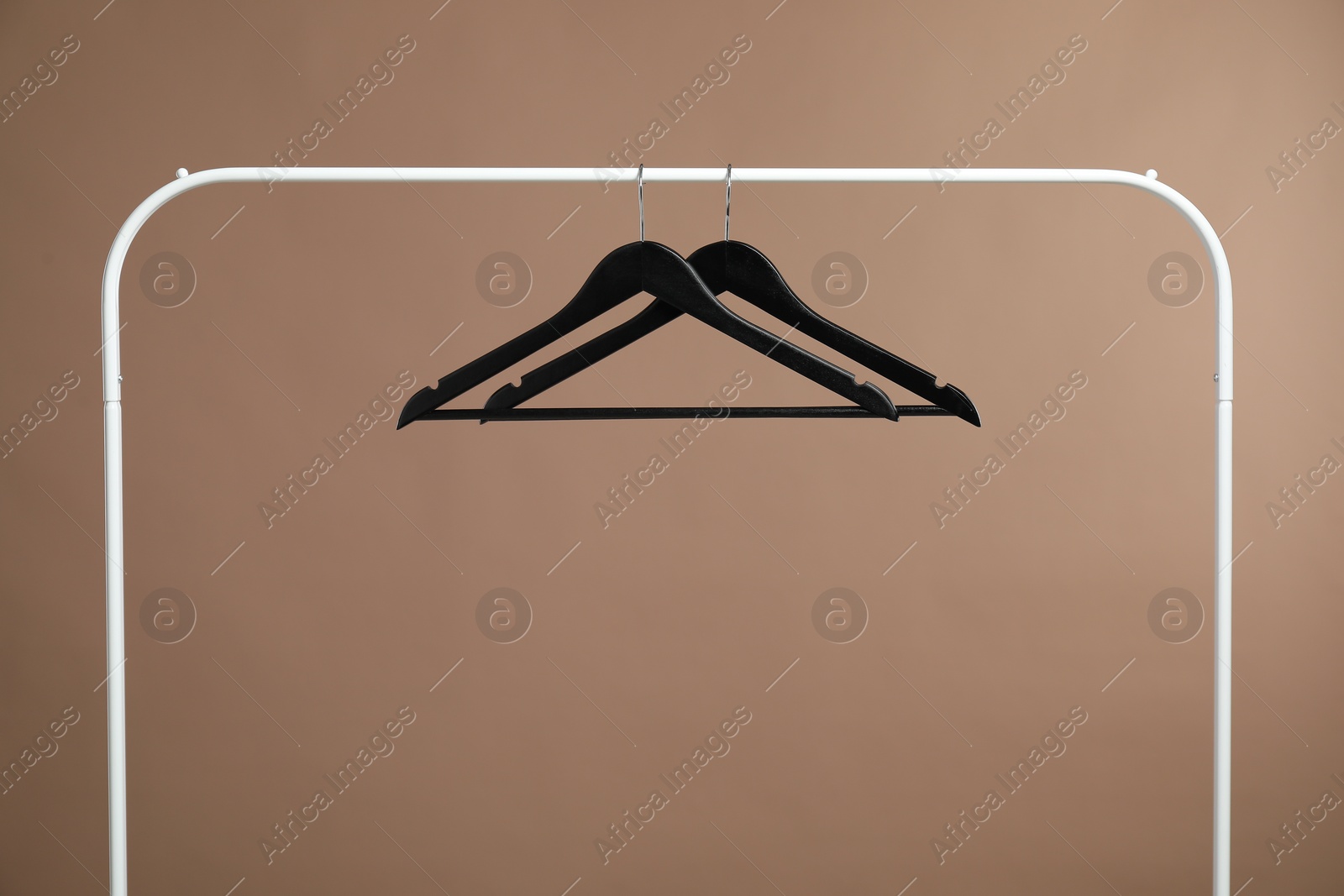 Photo of Black clothes hangers on rack against light brown background