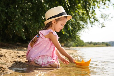 Photo of Cute little girl playing with paper boat near river