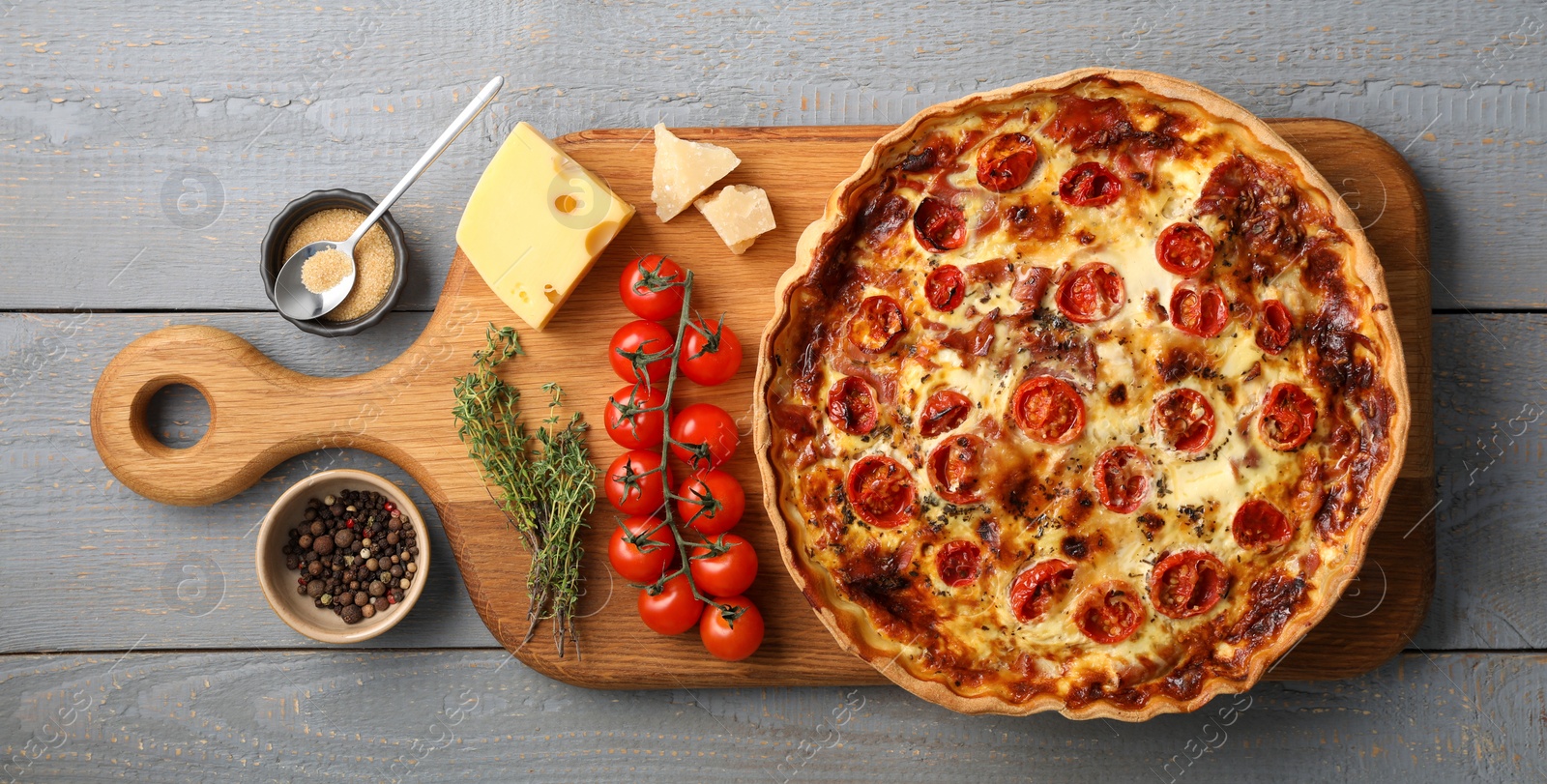 Photo of Delicious homemade prosciutto quiche and ingredients on gray wooden table, flat lay