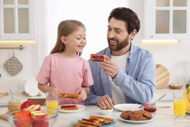 Father and his cute little daughter having breakfast at table in kitchen