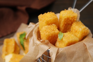 Photo of Tasty fried mozzarella sticks in metal basket, closeup
