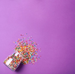 Photo of Jar with colorful sprinkles and space for text on purple background, flat lay. Confectionery decor
