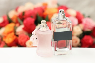 Photo of Bottles of perfume on white table against beautiful roses, closeup