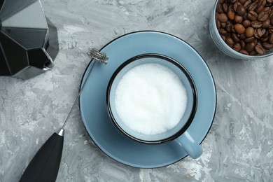 Mini mixer (milk frother), whipped milk in cup, coffee beans and moka pot on grey textured table, flat lay