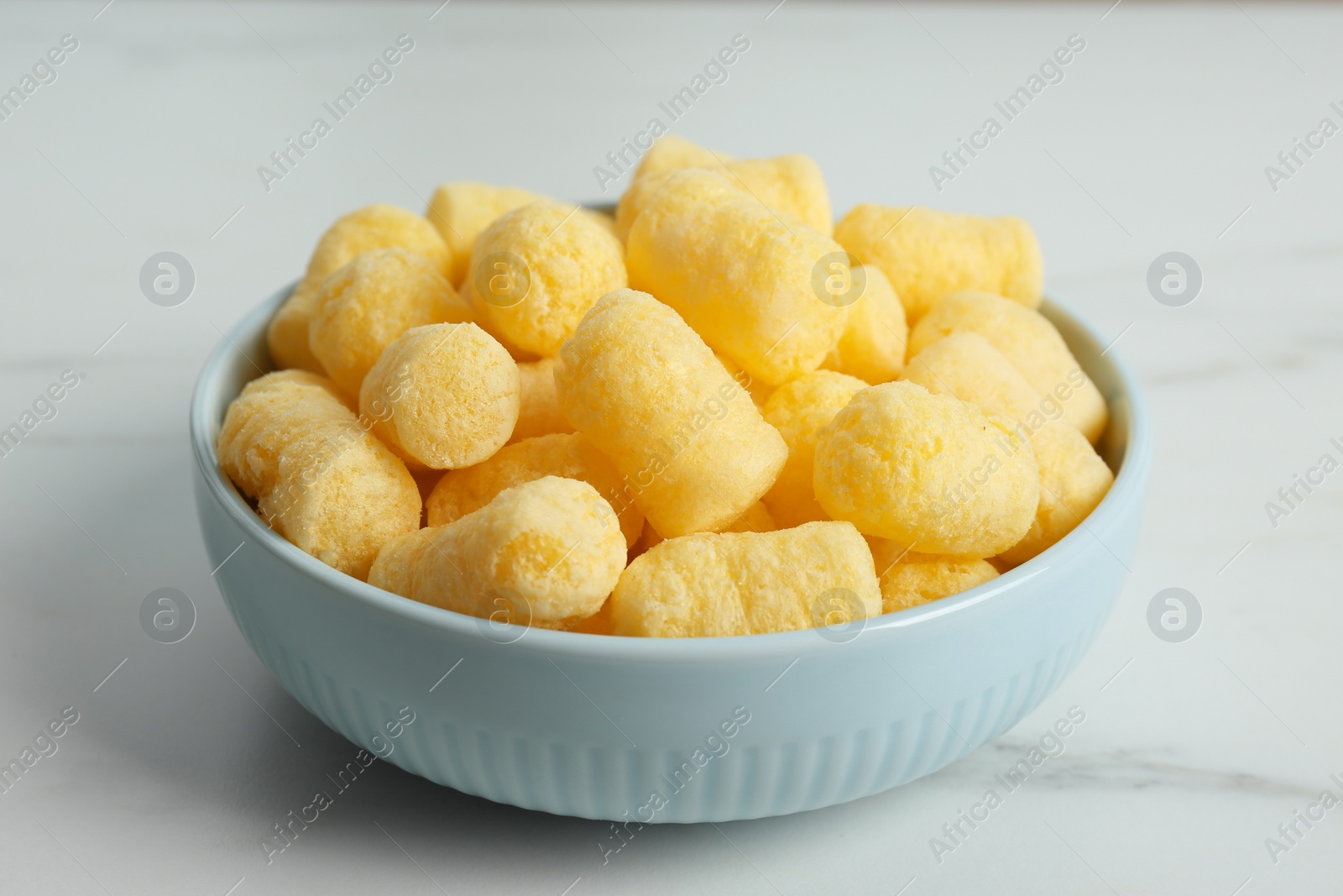 Photo of Bowl of delicious crispy corn sticks on white marble table