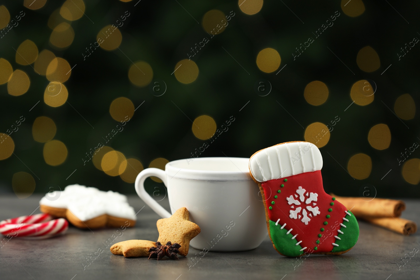 Photo of Decorated cookies and hot drink on grey table against blurred Christmas lights