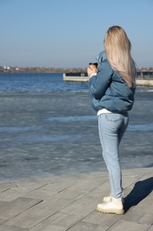 Lonely woman with cup of drink on pier near river, back view