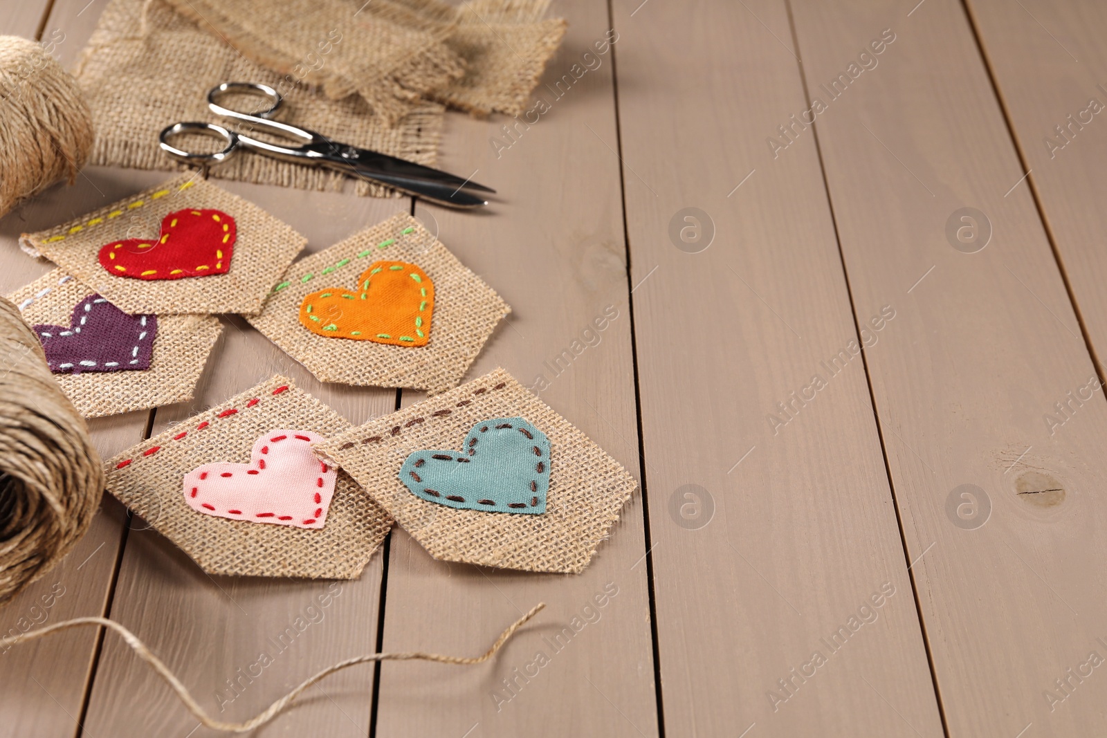 Photo of Pieces of burlap fabric with hearts and scissors on wooden table, space for text