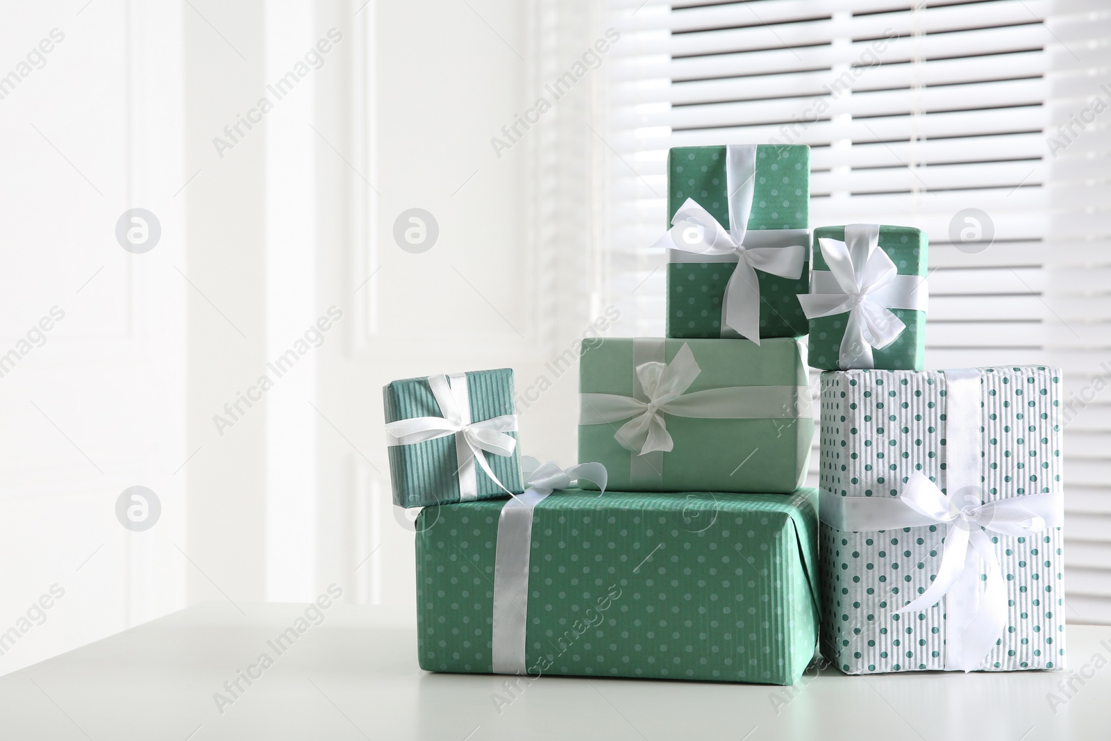 Photo of Heap of wrapped gift boxes on white table, space for text. Happy holiday