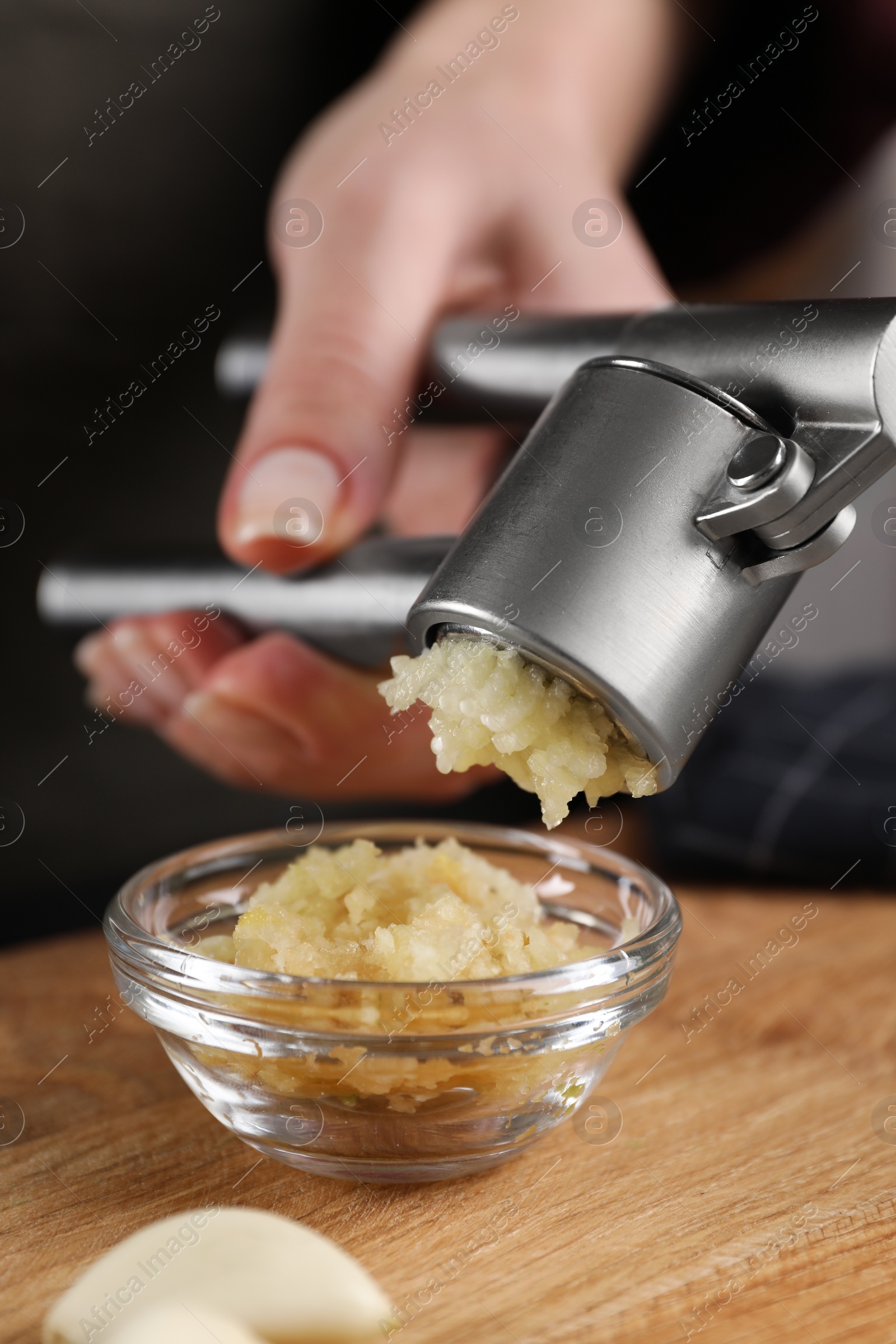 Photo of Woman squeezing garlic with press at wooden table, closeup