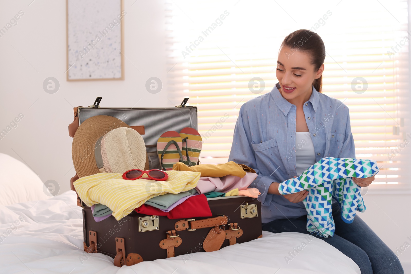 Photo of Woman packing suitcase for summer vacation in bedroom