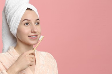 Portrait of smiling woman with dental braces and toothbrush on pink background. Space for text