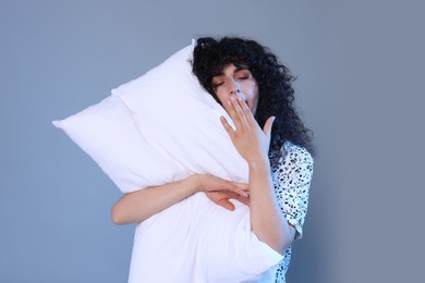 Photo of Tired young woman with pillow yawning on light grey background. Insomnia problem