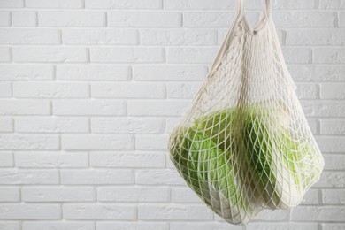 Photo of Woman holding string bag with fresh Chinese cabbages near white brick wall, closeup. Space for text