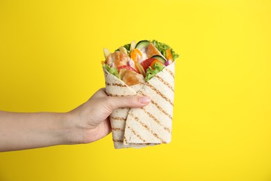 Photo of Woman holding delicious chicken shawarma on yellow background, closeup