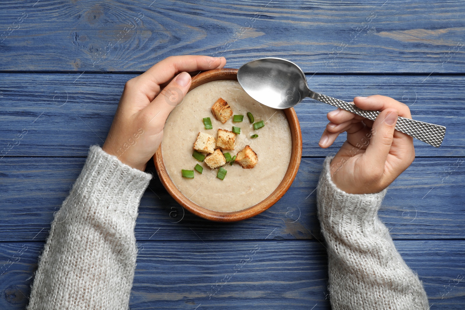 Photo of Woman eating fresh homemade mushroom soup from bowl on table, top view