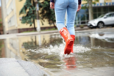 Photo of Woman with red rubber boots in puddle, closeup. Rainy weather