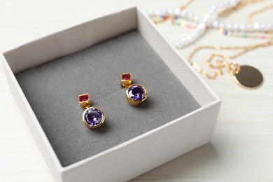 Photo of Earrings in jewel box on white wooden table, closeup