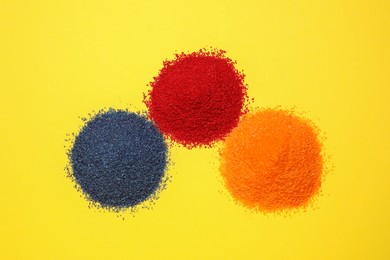 Heaps of different bright food coloring on yellow background, flat lay