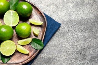 Photo of Fresh ripe limes and leaves on grey table, top view. Space for text