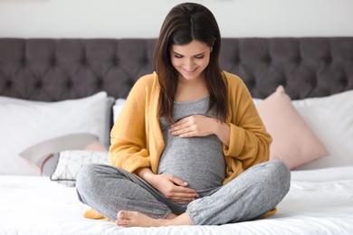 Young pregnant woman sitting on bed at home