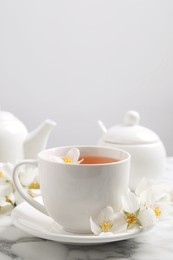 Photo of Aromatic jasmine tea and fresh flowers on white marble table, space for text