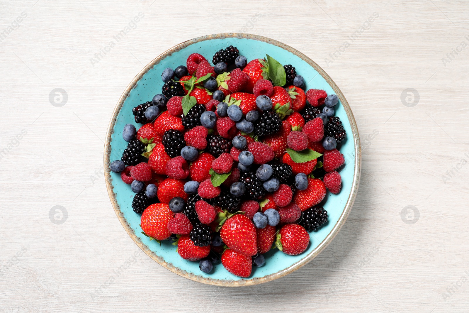 Photo of Many different fresh ripe berries in bowl on white wooden table, top view