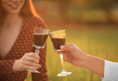 Photo of Happy young couple clinking wineglasses in park, closeup. Picnic season