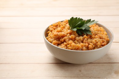 Delicious red lentils with parsley in bowl on wooden table, closeup. Space for text