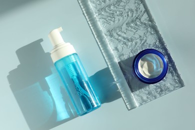 Photo of Bottle and jar of cosmetic products on light blue background, flat lay