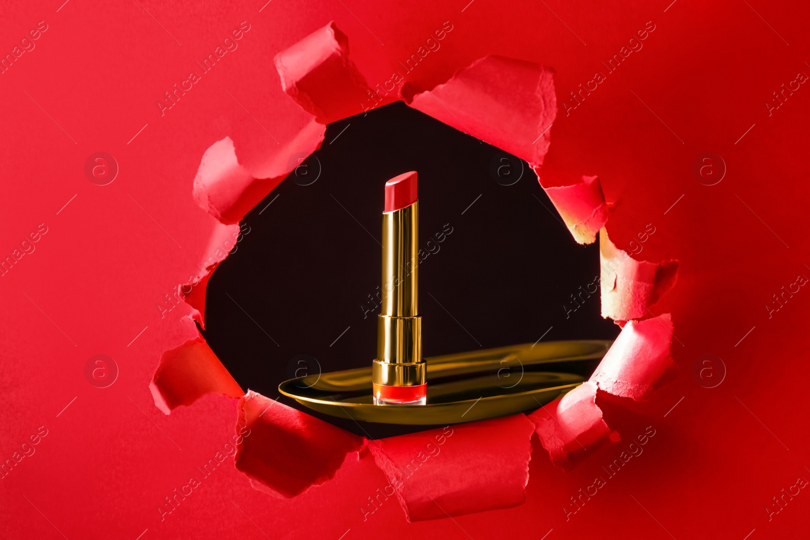 Photo of Bright red lipstick on gold plate, view through hole in paper