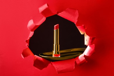 Photo of Bright red lipstick on gold plate, view through hole in paper