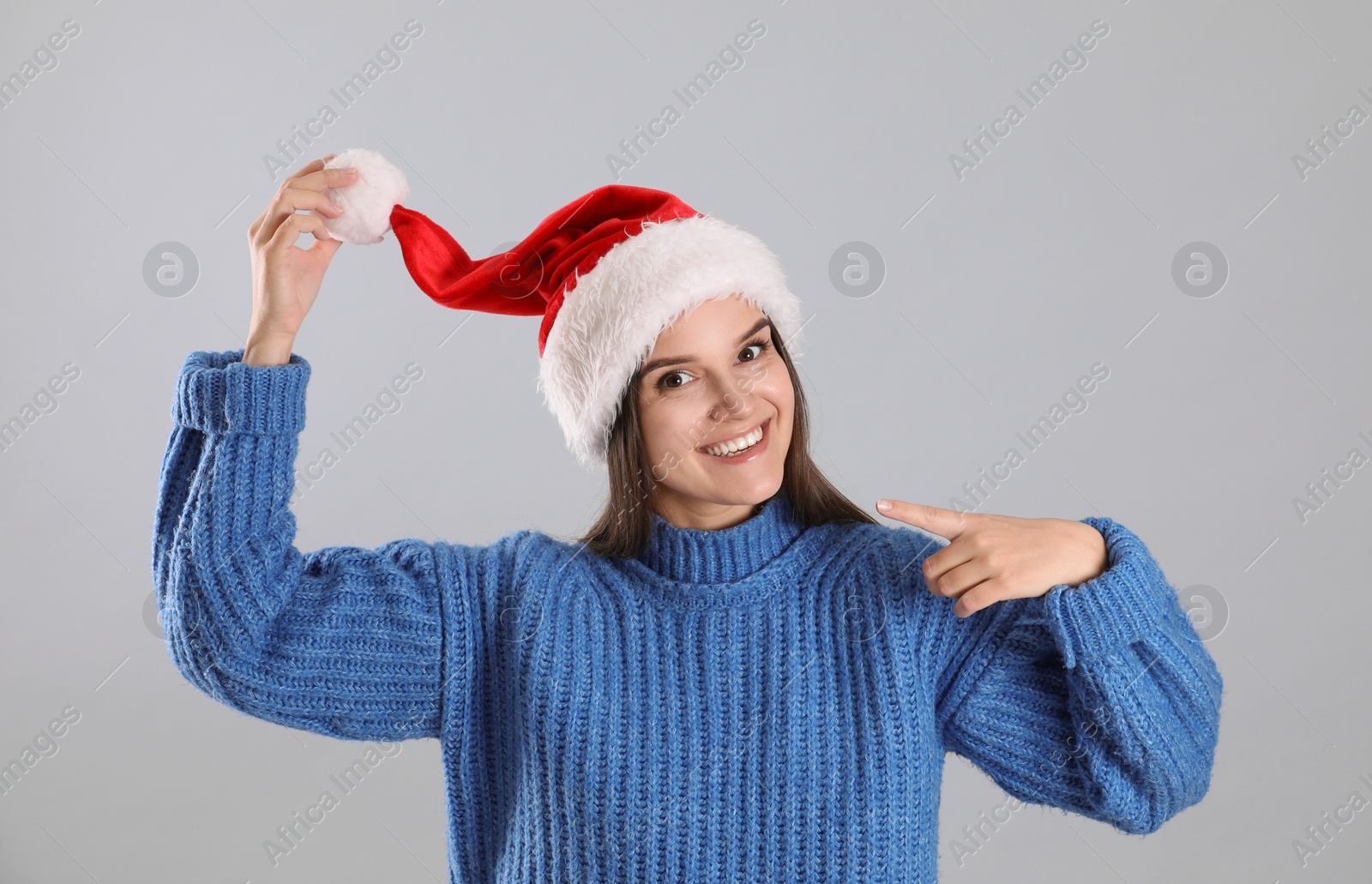 Photo of Pretty woman in Santa hat and blue sweater on grey background