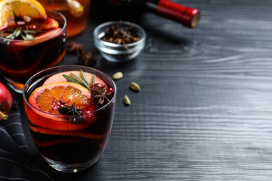 Photo of Cup of tasty mulled wine on black wooden table. Space for text