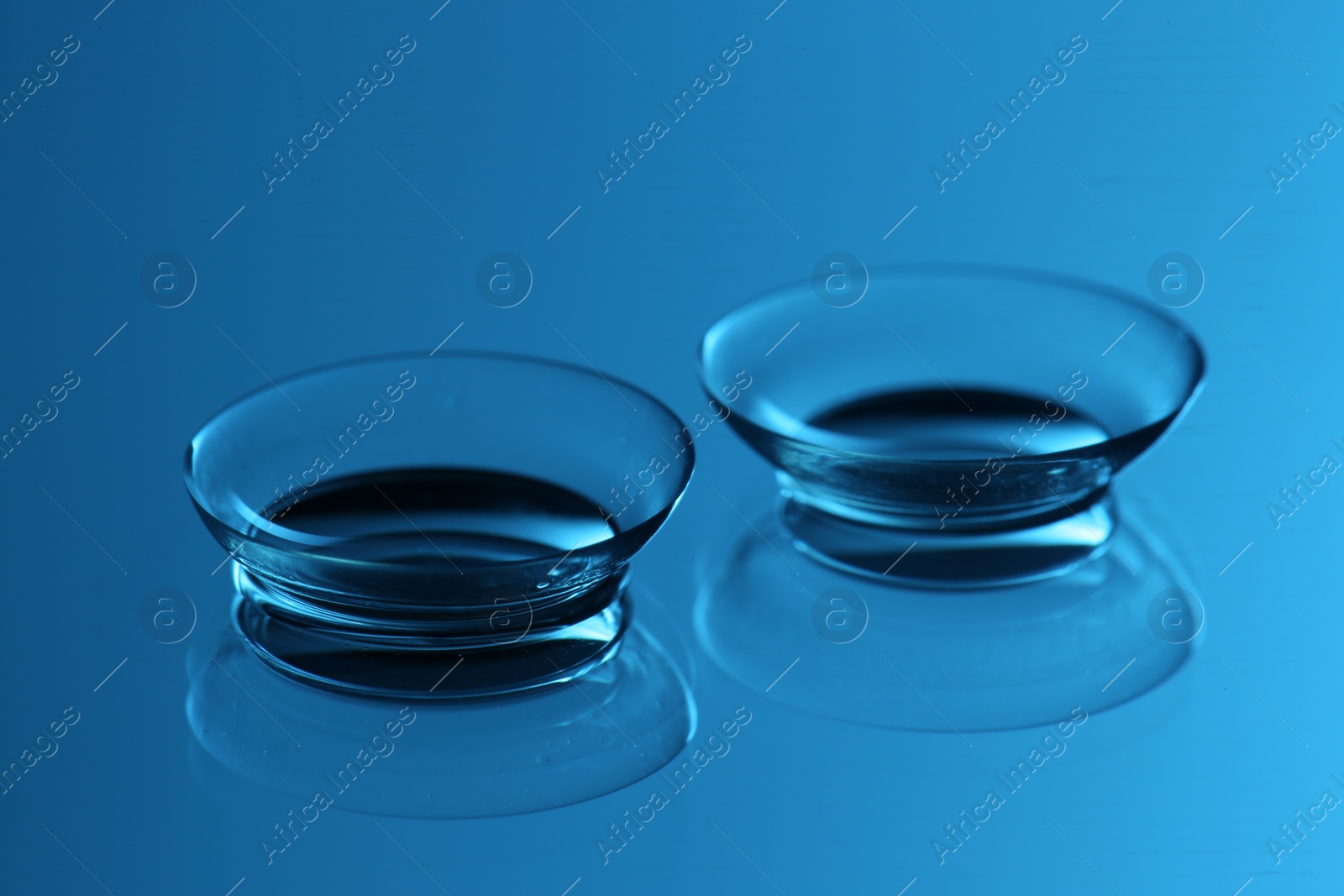 Photo of Pair of contact lenses on mirror surface, closeup. Toned in blue