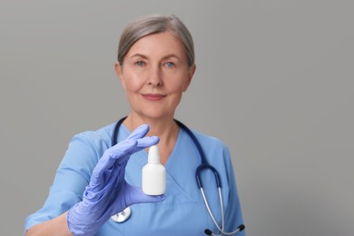 Photo of Woman holding nasal spray against light grey background, focus on bottle