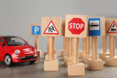 Photo of Many different miniature road signs and car on grey table, closeup. Driving school