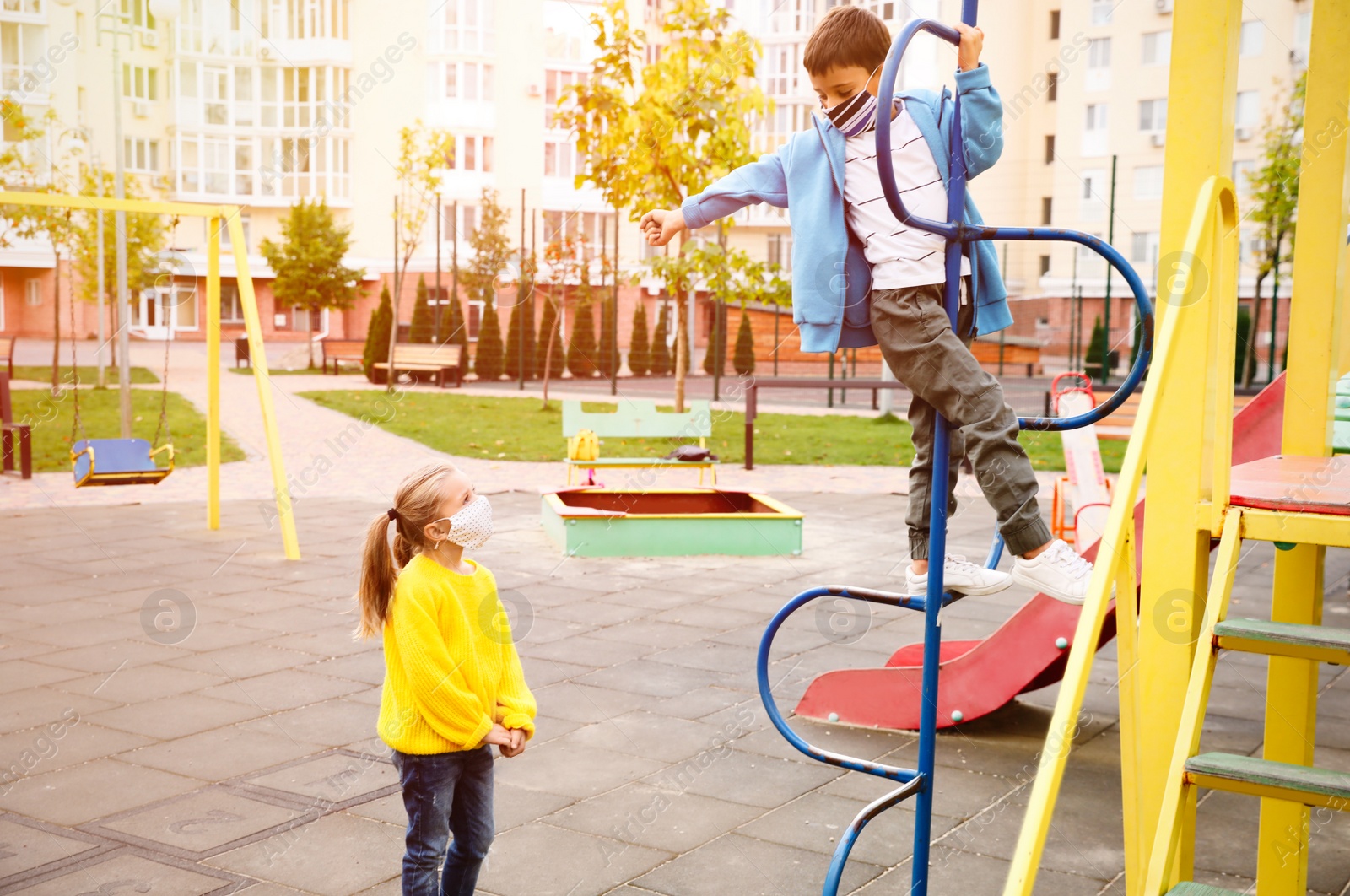 Photo of Little children with medical face masks on playground during covid-19 quarantine