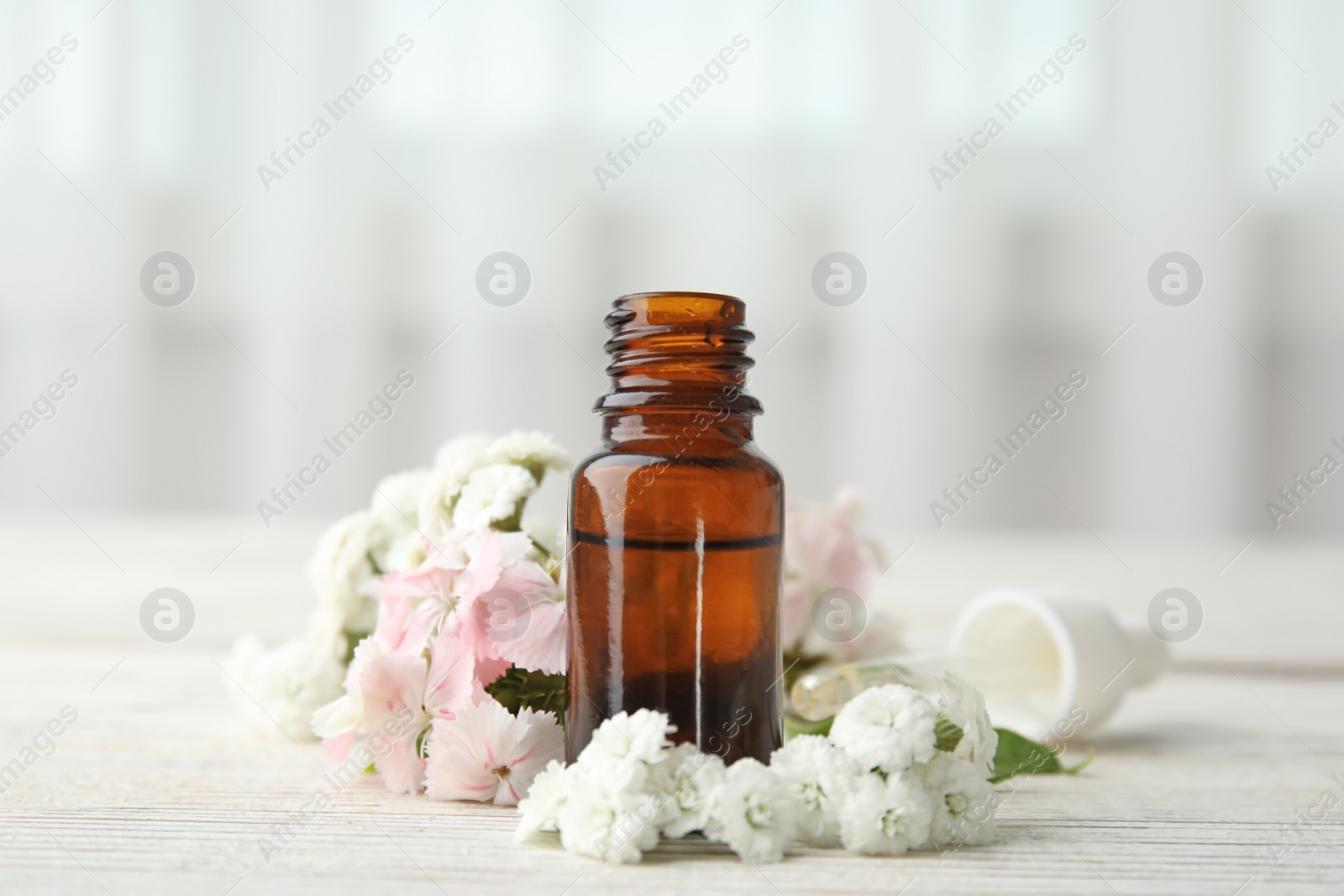 Photo of Bottle of essential oil and flowers on table