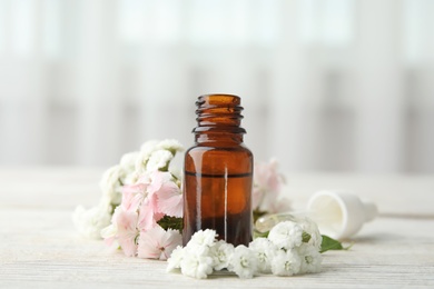 Bottle of essential oil and flowers on table