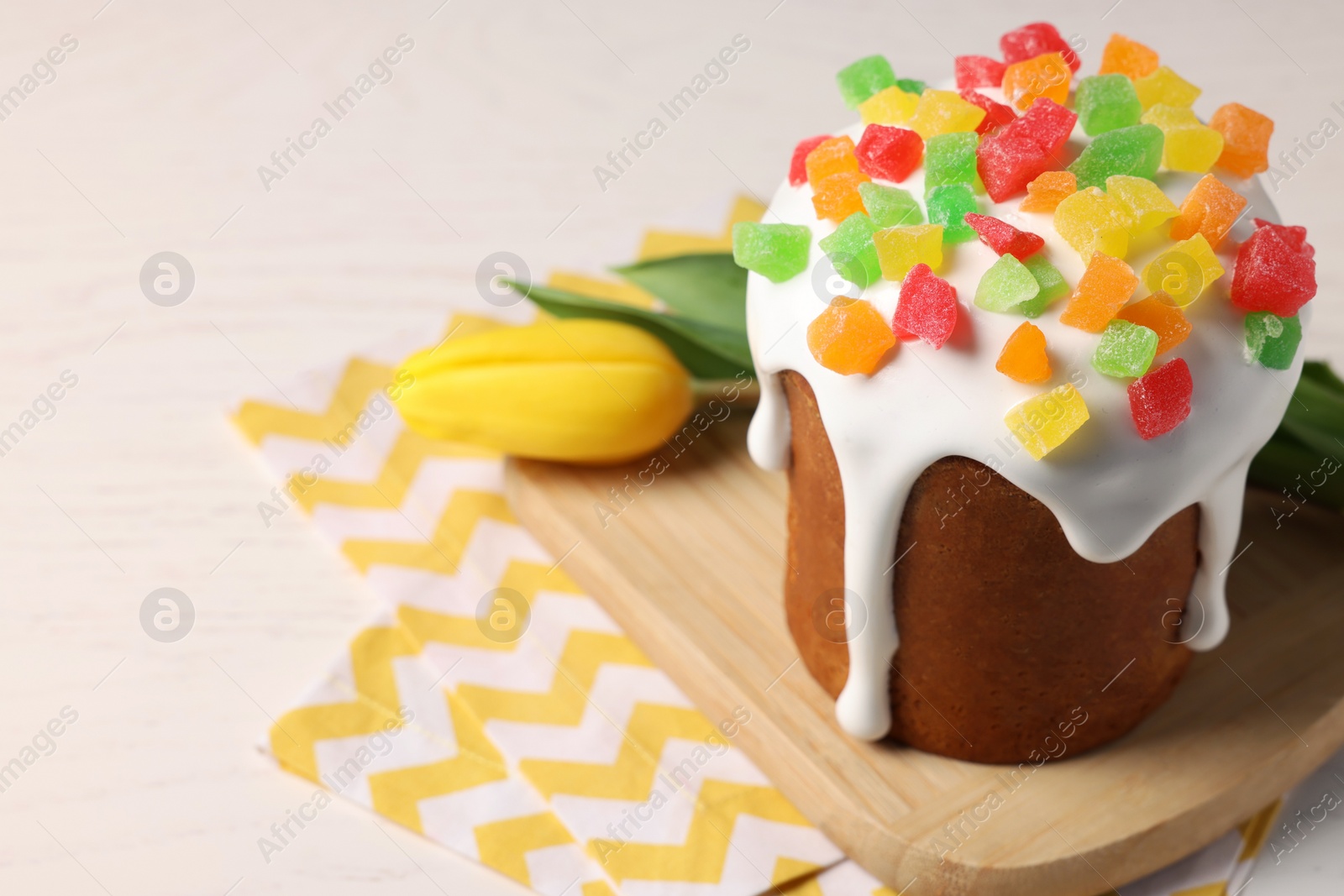 Photo of Delicious Easter cake with pieces of candied fruits and tulip on white table, closeup. Space for text